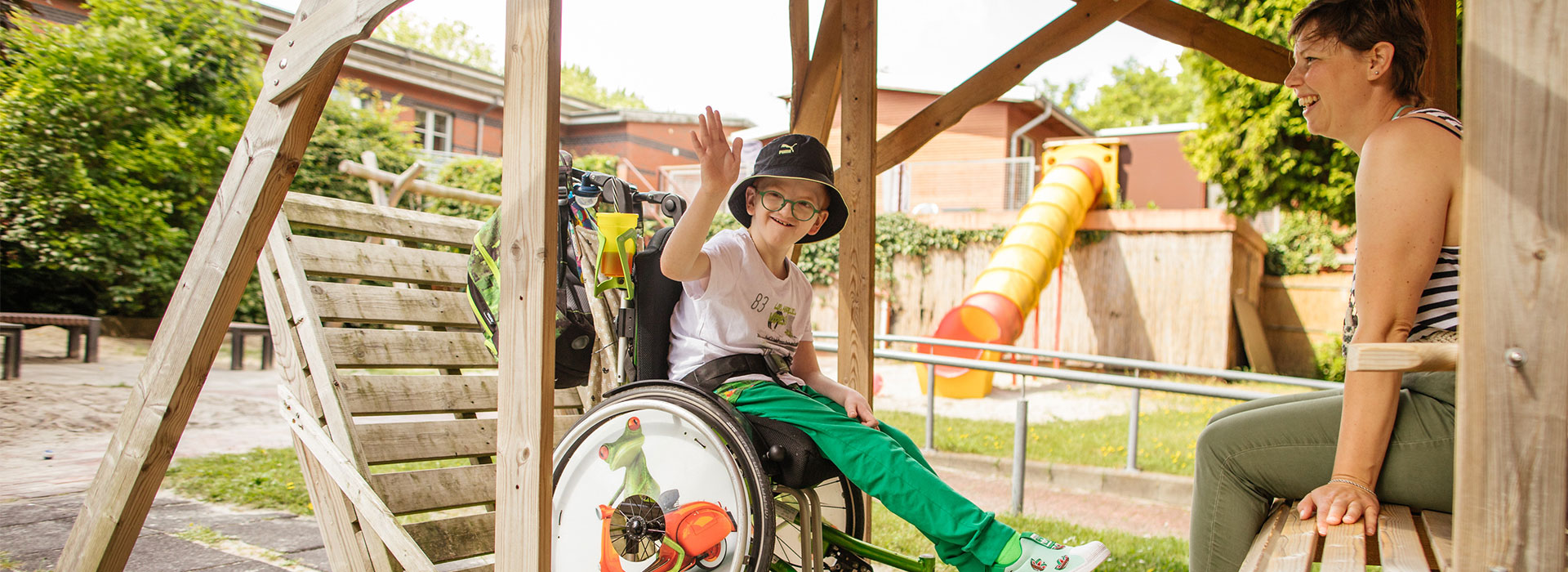 Junge mit Hut im Rollstuhl winkt